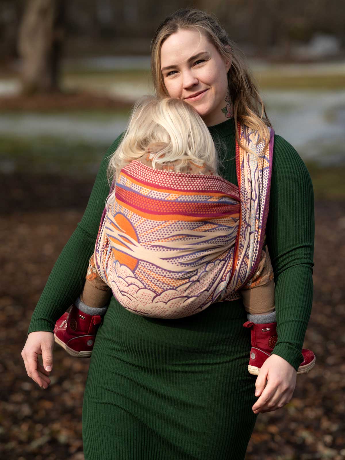 Woman carrying a child in a patterned baby wrap outdoors.
