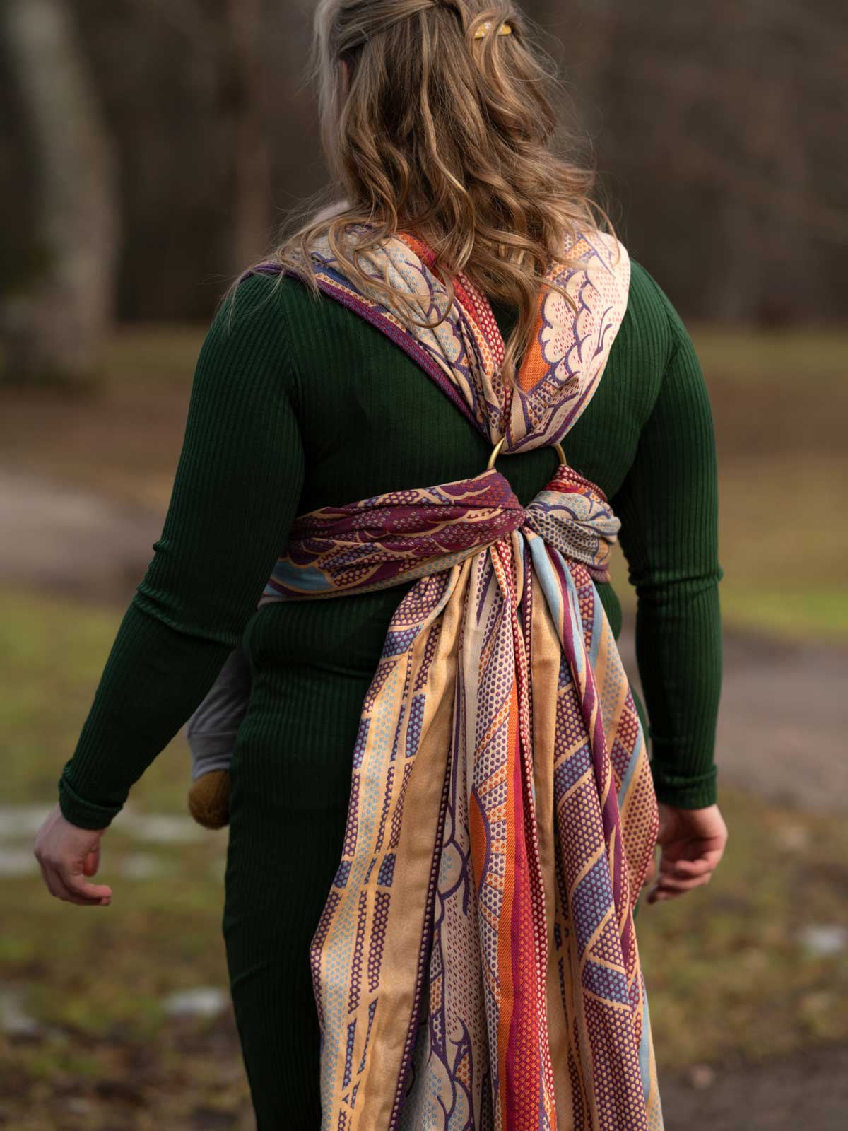 Person wearing a green sweater and a colorful patterned woven wrap outdoors.