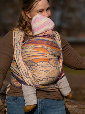 Woman wearing a baby in a colorful woven wrap with a blurred natural background
