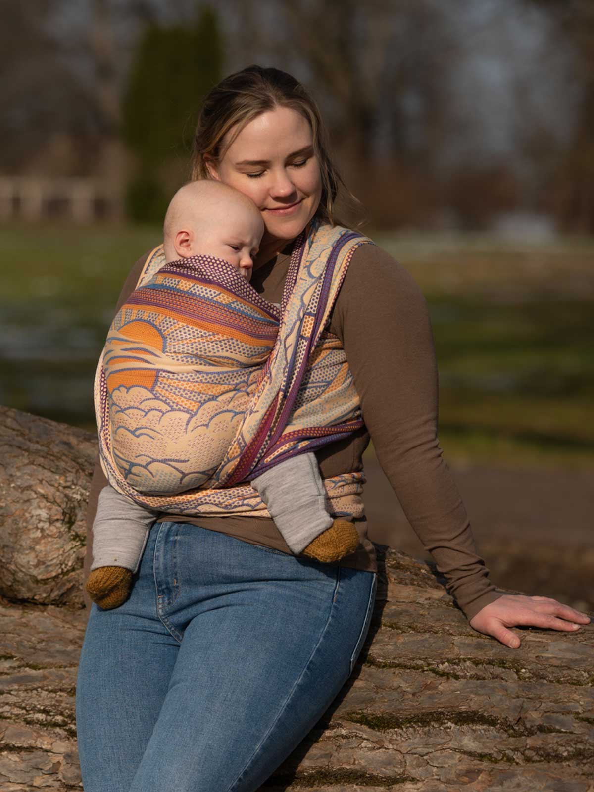 Woman holding a baby wrapped in a colorful sling outdoors