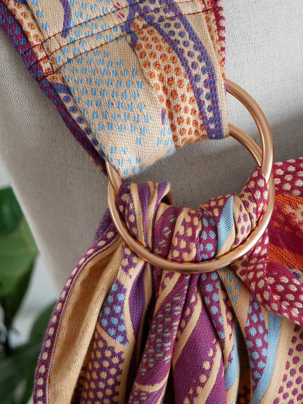 Patterned fring sling with a gold ring tied around it against a neutral background