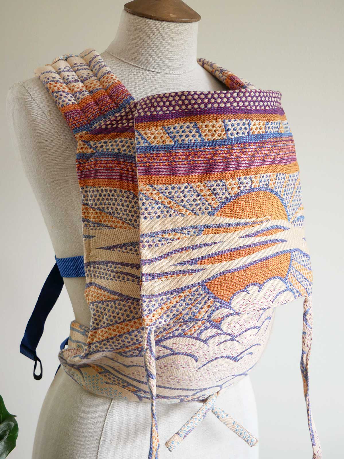 Colorful baby carrier on a mannequin against a plain background