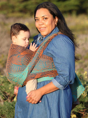 Side view of model carrying baby in fox pattered baby wrap. 